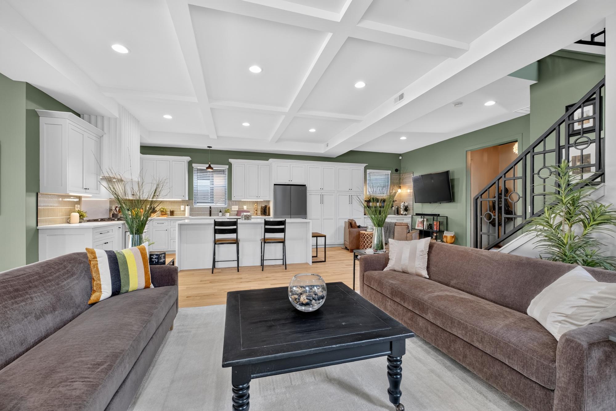 Open living room with fresh gray and sage walls, white coffered ceiling and kitchen beyond