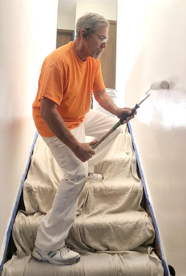 Dan Utter rolling paint in a stairwell with the steps covered in drop cloths