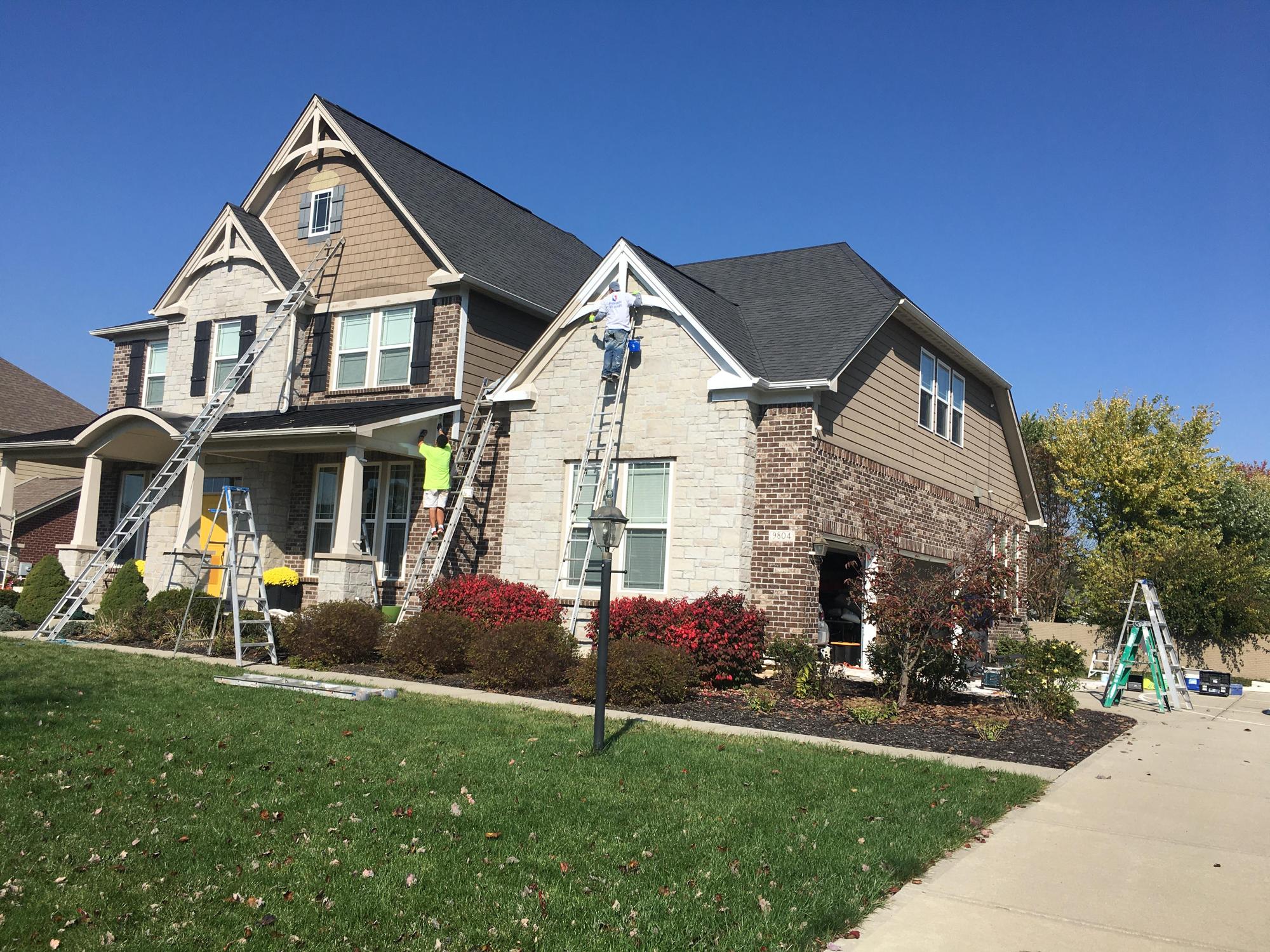 Dru's Hues crew on ladders painting the exterior of a stone and siding home